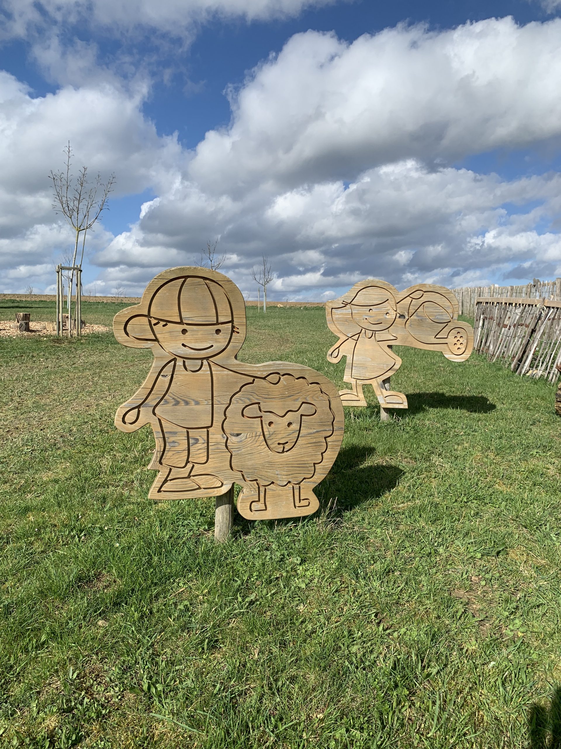 Holzfiguren von Kindern mit Schaf auf der Wiese